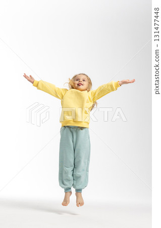 Portrait of beautiful cute little toddler girl. Child with funny face in yellow sweatshirt jumps. Pretty smile kid in studio on white background. High quality photo 131477448
