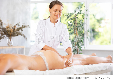 Young woman masseuse doing massage of thighs and buttocks 131477479