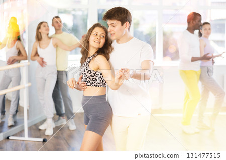 Happy young woman dressed in sportswear with man dancing bachata during group dance lesson in ballroom dance class 131477515