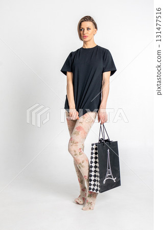 Woman in light tights and black T-shirt with black gift bag in French style on light background. Vertical photo. High quality photo Woman in light tights and black T-shirt with black gift bag in French style on light background. Vertical photo. High quality photo 131477516