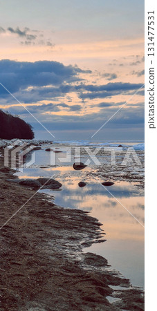 Peaceful scene of ice floes drifting in calm ocean waters with stunning sunset sky. Reflective water surface captures colorful clouds, evoking serenity and tranquility. Vertical photo 131477531