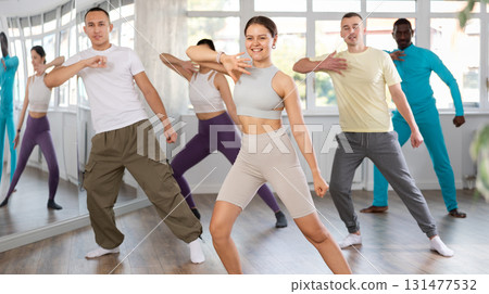 Happy girl and group of multinational young people practicing new modern dance techniques at dance school 131477532