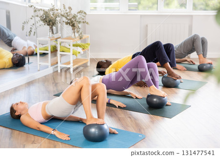 Sporty girl doing glute bridge with ball at group Pilates class Sporty girl doing glute bridge with ball at group Pilates class 131477541