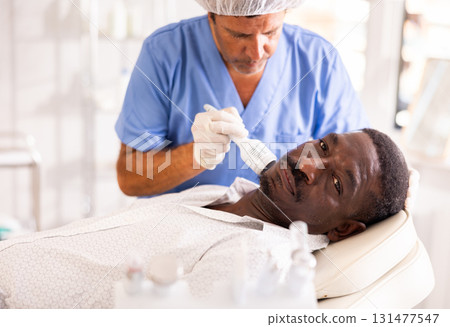 African man client undergoes facial skin care procedure using nozzle cold hammer whitening African man client undergoes facial skin care procedure using nozzle cold hammer whitening 131477547
