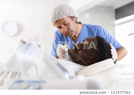 Male cosmetologist performs skin cleansing procedure for African man client with beauty machine 131477561