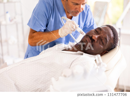 African man receiving facial cleansing with hydrogen and oxygen ions attachment 131477706