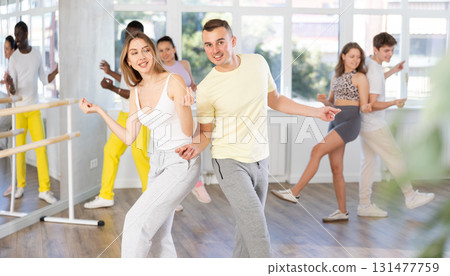 Happy young woman and man with group of multinational people enjoying active boogie-woogie dance in studio 131477759