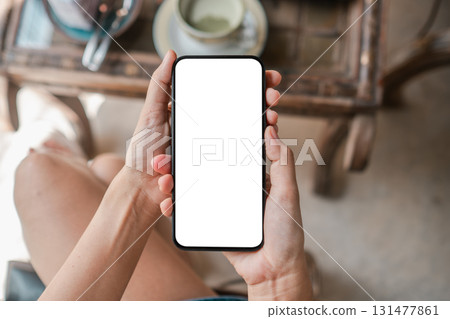 Close-up of hands holding a smartphone with a blank screen in a cafe, ideal for app mockups or digital content. 131477861