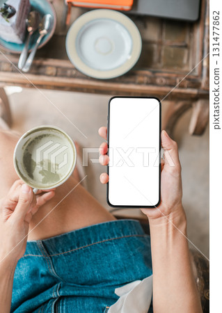 Overhead view of a woman holding a coffee cup and smartphone with a blank screen, ready for customization. 131477862