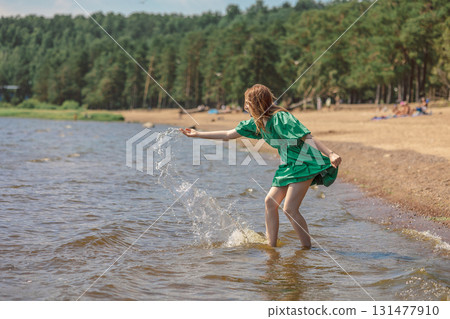 Happy teenage girl walking along coastline.Girl playing with water, splashing on beach on holidays. High quality photo 131477910