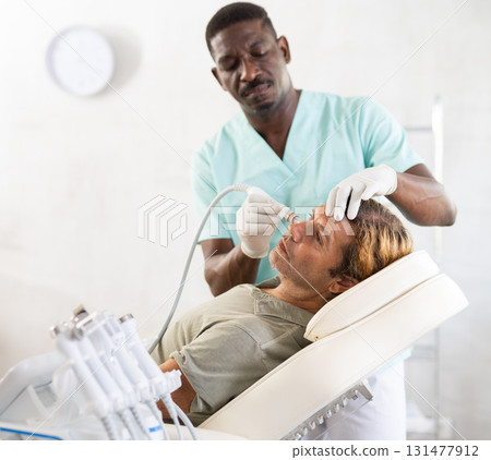 African male cosmetologist performs skin cleansing procedure for man client with beauty machine 131477912