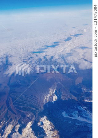 View from window of plane to blue sky and snowy mountain peaks in white clouds. High quality photo 131478094