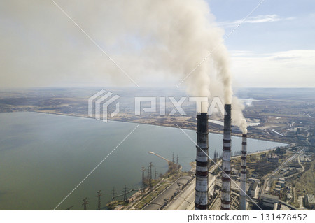 Tall pipes of power plant, white smoke on rural landscape, lake water and blue sky copy space background. 131478452