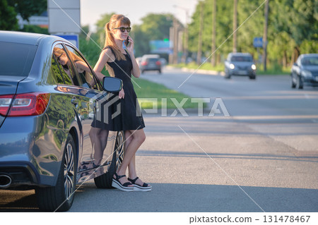 Stylish woman driver standing near her vehicle talking on cellphone on city street in summer Stylish woman driver standing near her vehicle talking on cellphone on city street in summer 131478467