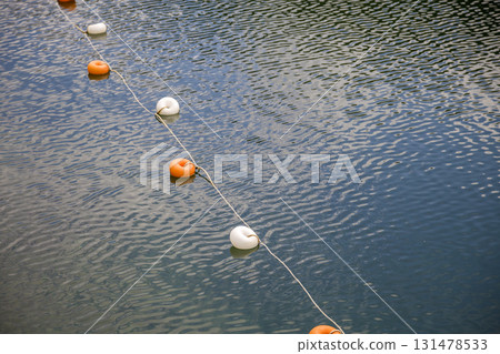 Rope with white and yellow restriction markers on water surface for prohibiting of swimming in deep lake or sea. 131478533