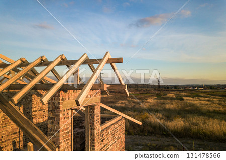 Private residential house with wooden roof frame structure under construction. Unfinished brick building under development. Private residential house with wooden roof frame structure under construction. Unfinished brick building under development. 131478566