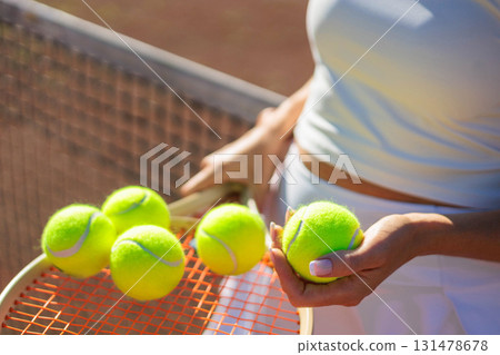 Woman tennis player hands holding yellow balls on racket at summer sunset outdoor court closeup Woman tennis player hands holding yellow balls on racket at summer sunset outdoor court closeup 131478678