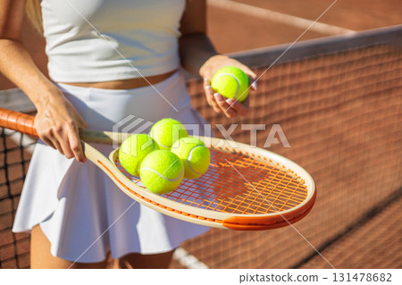 Woman tennis player hands holding yellow balls on racket at summer sunset outdoor court closeup 131478682