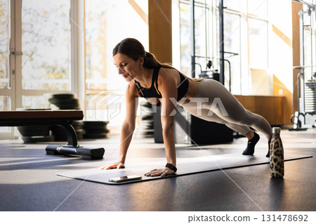 Smiling fitness woman stand in plank position doing push ups training at gym Smiling fitness woman stand in plank position doing push ups training at gym 131478692