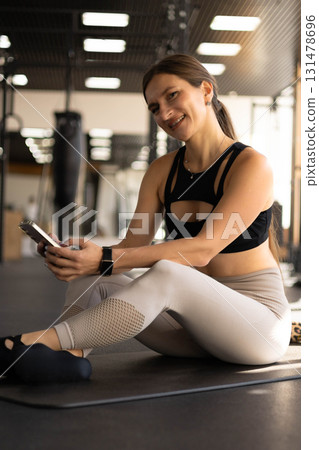 Fitness woman relaxing on mat use smartphone chatting at gym enjoy break Fitness woman relaxing on mat use smartphone chatting at gym enjoy break 131478696