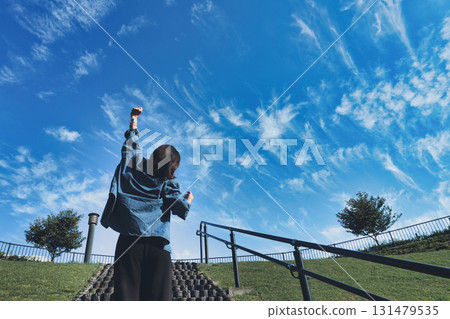A woman's back view posing in a fist pump against the blue sky 131479535