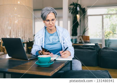 Focused senior woman with gray hair writing notes during menopause in active 131480341
