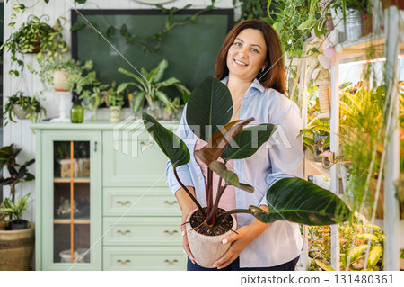 Smiling woman florist gardener with philodendron at indoor home garden closeup Smiling woman florist gardener with philodendron at indoor home garden closeup 131480361