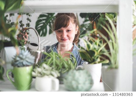 A young woman enjoys caring for flowers. Watering indoor plants and admiring them. A young woman enjoys caring for flowers. Watering indoor plants and admiring them. 131480363