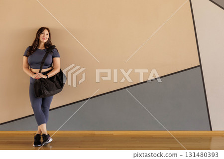Full figured woman in activewear carrying gym bag in bright studio after yoga workout 131480393