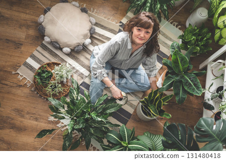 A young woman enjoys caring for flowers. Watering indoor plants and admiring them. A young woman enjoys caring for flowers. Watering indoor plants and admiring them. 131480418