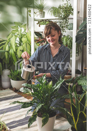 A young woman enjoys caring for flowers. Watering indoor plants and admiring them.  131480422