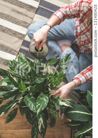 A young woman enjoys caring for flowers. Watering indoor plants and admiring them. 131480428