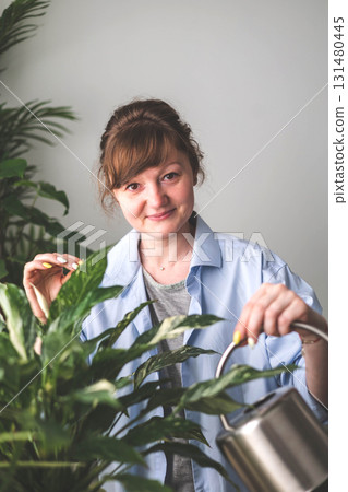 A young woman enjoys caring for flowers. Watering indoor plants and admiring them.  131480445