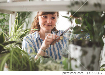 A young woman enjoys caring for flowers. Watering indoor plants and admiring them. 131480447