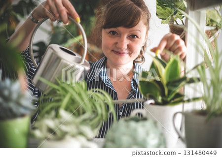 A young woman enjoys caring for flowers. Watering indoor plants and admiring them. 131480449