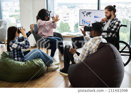 Group of diverse adults using virtual reality headsets and laptops in modern office setting. Individuals of various backgrounds collaborating in technology-driven workspace fostering creativity 131481096