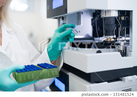 Scientist in rubber gloves carefully loading vial into autosampler for chemical, pharmaceutical, and clinical testing procedures Scientist in rubber gloves carefully loading vial into autosampler for chemical, pharmaceutical, and clinical testing procedures 131481524