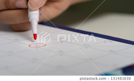 Close up of hand circling date on calendar with red marker, symbolizing appointment, or reminder Close up of hand circling date on calendar with red marker, symbolizing appointment, or reminder 131481630