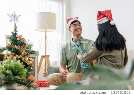 Christmas celebration shows happy couple sharing love at home, woman adjusting man tie, enjoying winter holiday festive spirit near decorated christmas tree, cozy day. Christmas celebration shows happy couple sharing love at home, woman adjusting man tie, enjoying winter holiday festive spirit near decorated christmas tree, cozy day. 131481901