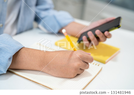 Teenage write in notebook and use mobile phone search data online to online learning university education. 131481946