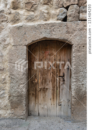 Weathered Wooden Door with Arched Stone Frame in an Ancient Stone Wall Weathered Wooden Door with Arched Stone Frame in an Ancient Stone Wall 131484293