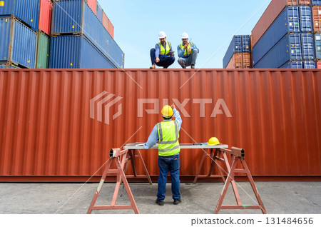 Container operator wearing white helmet and reflection shirt and holding tablet doing routine inspection while working in container yards. Logistics and shipping concept 131484656