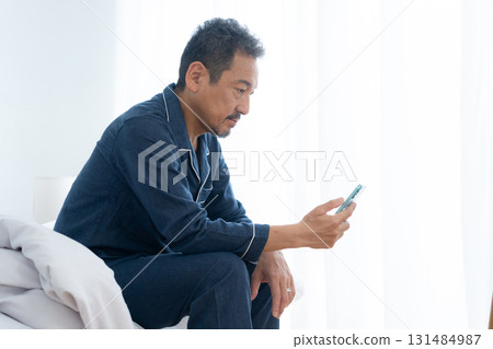 Middle-aged man looking at smartphone in bedroom Middle-aged man looking at smartphone in bedroom 131484987