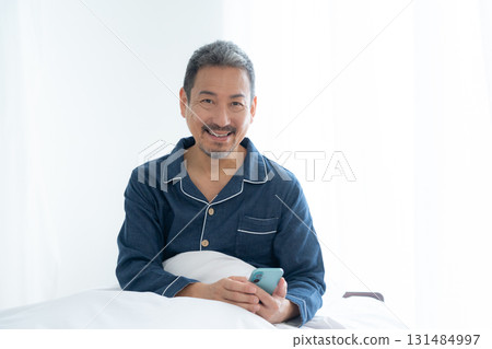 Middle-aged man looking at smartphone in bedroom Middle-aged man looking at smartphone in bedroom 131484997