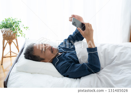 Middle-aged man looking at smartphone in bedroom Middle-aged man looking at smartphone in bedroom 131485026