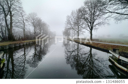 Breathtaking Misty Reflections on a Scenic Canal Surrounded by Bare Trees in the Morning Breathtaking Misty Reflections on a Scenic Canal Surrounded by Bare Trees in the Morning 131486055