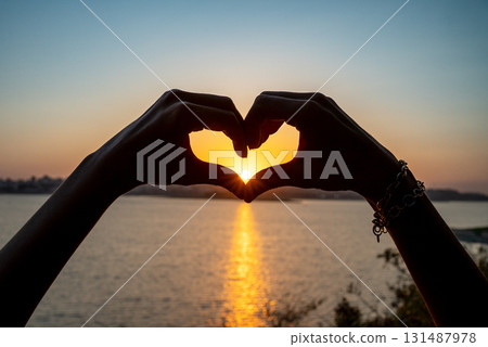 Silhouette of Hands Forming Heart Shape Around Sunset Over the Sea 131487978