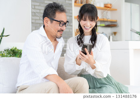 A middle-aged couple watching a smartphone in the living room A middle-aged couple watching a smartphone in the living room 131488176