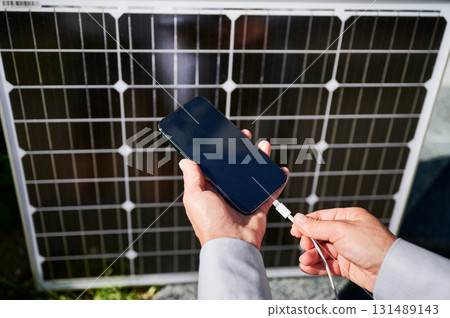 Close up view of woman charging her phone from solar battery. Female putting her mobile device on charge from solar panel. Integration of sustainable renewable energy into everyday life. Close up view of woman charging her phone from solar battery. Female putting her mobile device on charge from solar panel. Integration of sustainable renewable energy into everyday life. 131489143