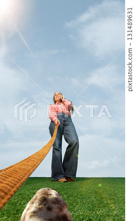 Woman walking with long orange leash and talking on phone from dog ground view Woman walking with long orange leash and talking on phone from dog ground view 131489631